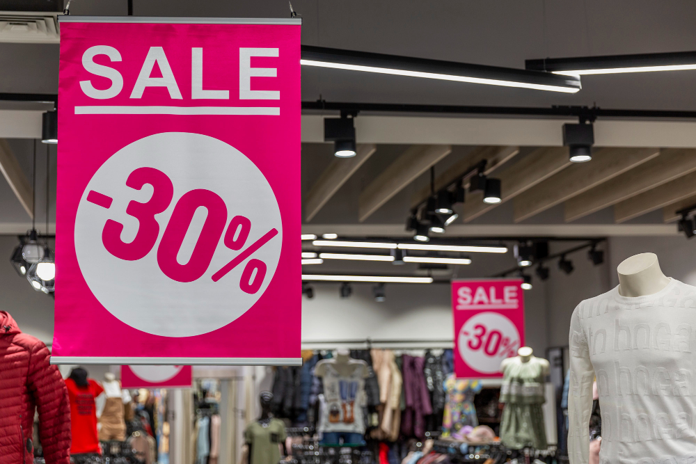 Cartaz promocional rosa em uma loja de roupas, com o texto “SALE -30%” em branco, indicando desconto de 30%.