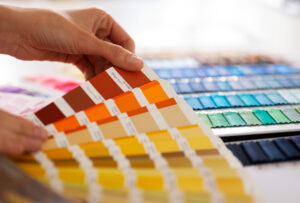 Pessoa manuseando catálogo de amostras de cores, com tons quentes em destaque e tecidos coloridos ao fundo.