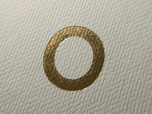 Círculo dourado em hot stamping sobre papel com textura leve.