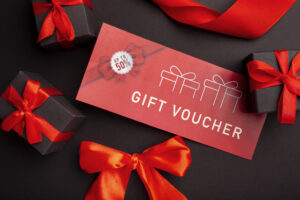 Vale-presente vermelho com a frase “Gift Voucher” e selo de desconto “Up to 50%”, cercado por caixas de presente pretas com laços vermelhos.